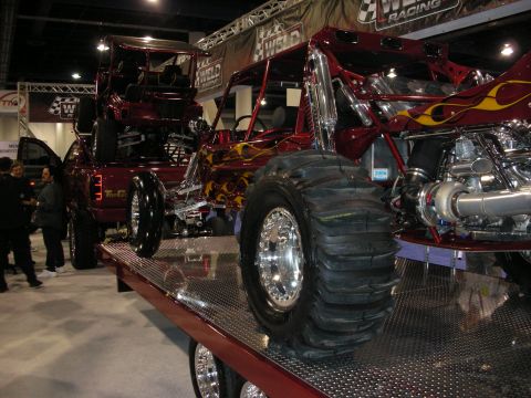 1998 Ford Crown Victoria - red flame-painted tube-chassis off-road buggy with paddle tires and a turbo engine sits on a display flatbed at a show.
