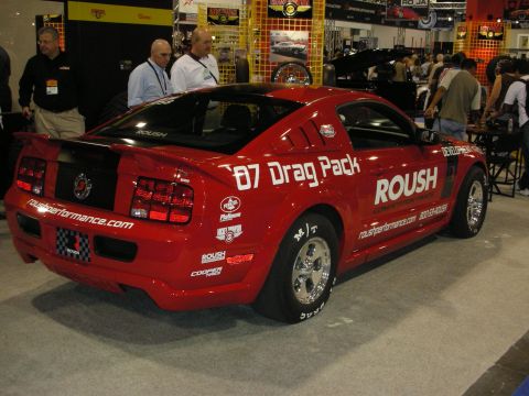 1998 Ford Crown Victoria - red Roush-liveried Ford Mustang badged '07 Drag Pack sits on display with drag wheels as attendees mingle behind it.