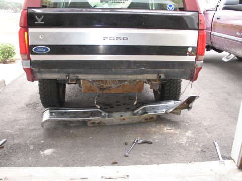 1995 Ford Bronco - The rear bumper of a 1995 Ford Bronco has been removed, with tools scattered nearby on the asphalt.