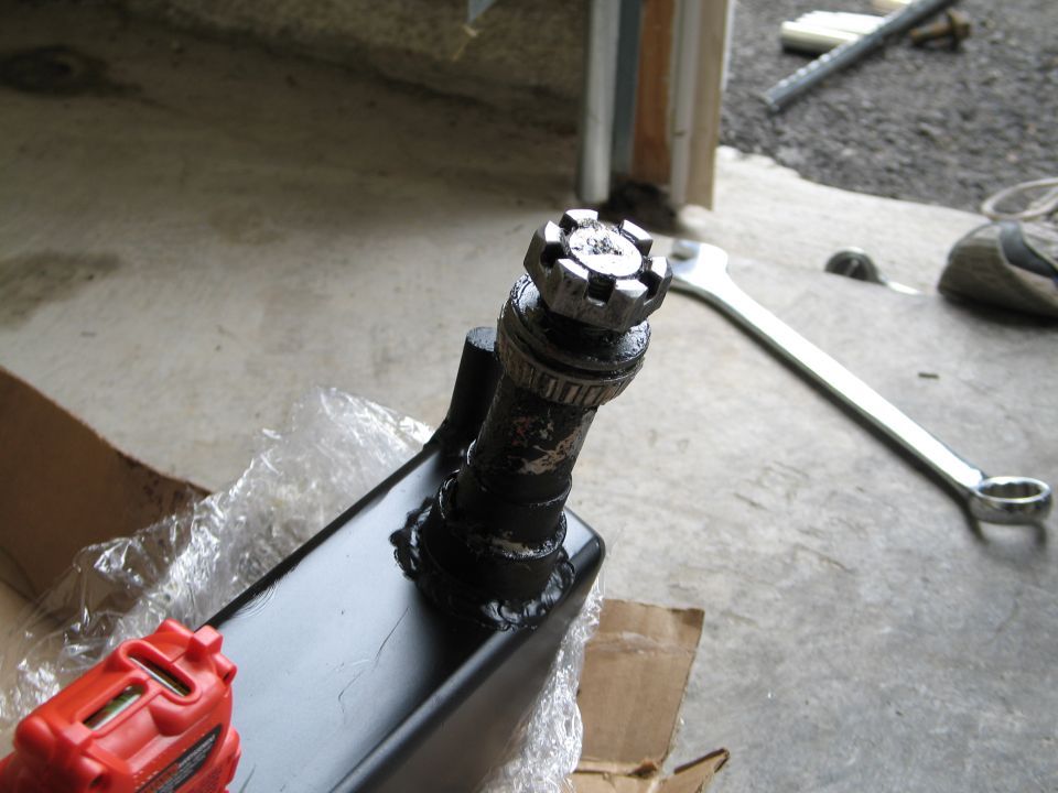 Black automotive part with a castle nut and a large wrench on a concrete floor