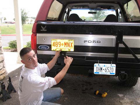 1995 Ford Bronco - A man is working on the rear bumper of a Ford Bronco, attaching a license plate.