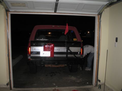 1995 Ford Bronco - A person works on the rear bumper of a Ford Bronco parked inside a garage at night.
