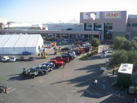 1998 Ford Crown Victoria - A wide view of the SEMA show parking lot, filled with various vehicles and a large exhibition tent.