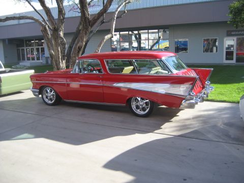 1998 Ford Crown Victoria - A classic red 1957 Chevrolet Nomad station wagon with chrome accents is parked on pavement.