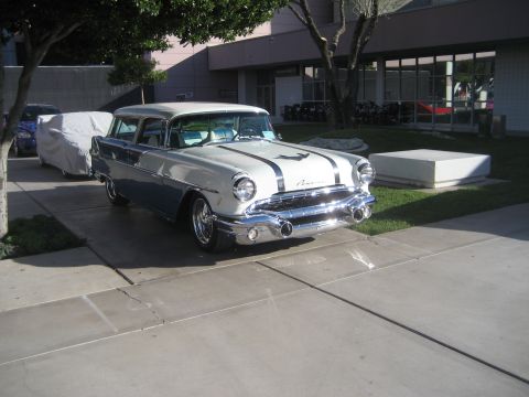 1998 Ford Crown Victoria - A classic 1957 Pontiac Chieftain Station Wagon is parked outside a building, with another vehicle covered in a tarp behind it.