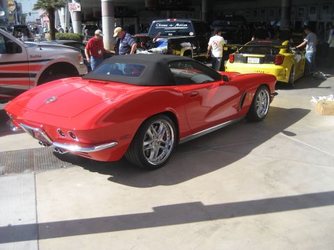 1998 Ford Crown Victoria - A red convertible sports car is parked outdoors with other vehicles and people in the background.
