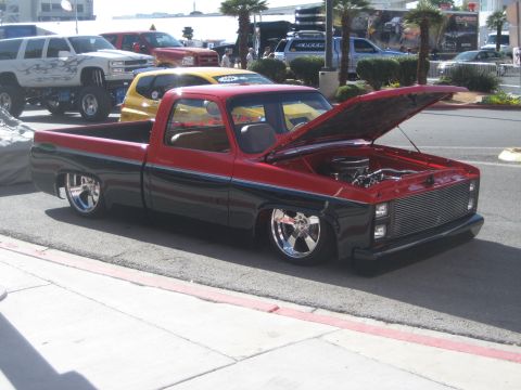 1998 Ford Crown Victoria - A two-tone pickup truck is parked on the street with its hood open, revealing the engine bay and custom chrome wheels.