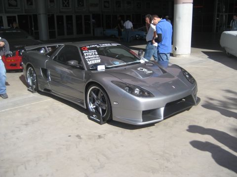 1998 Ford Crown Victoria - A modified silver sports car is displayed outdoors, with other vehicles and people in the background.