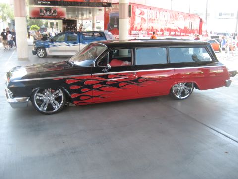 1998 Ford Crown Victoria - This custom station wagon features a striking flame paint job and large chrome wheels, parked alongside other vehicles.