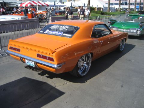 1998 Ford Crown Victoria - A custom orange 1969 Chevrolet Camaro is displayed outdoors, with a green classic convertible nearby.