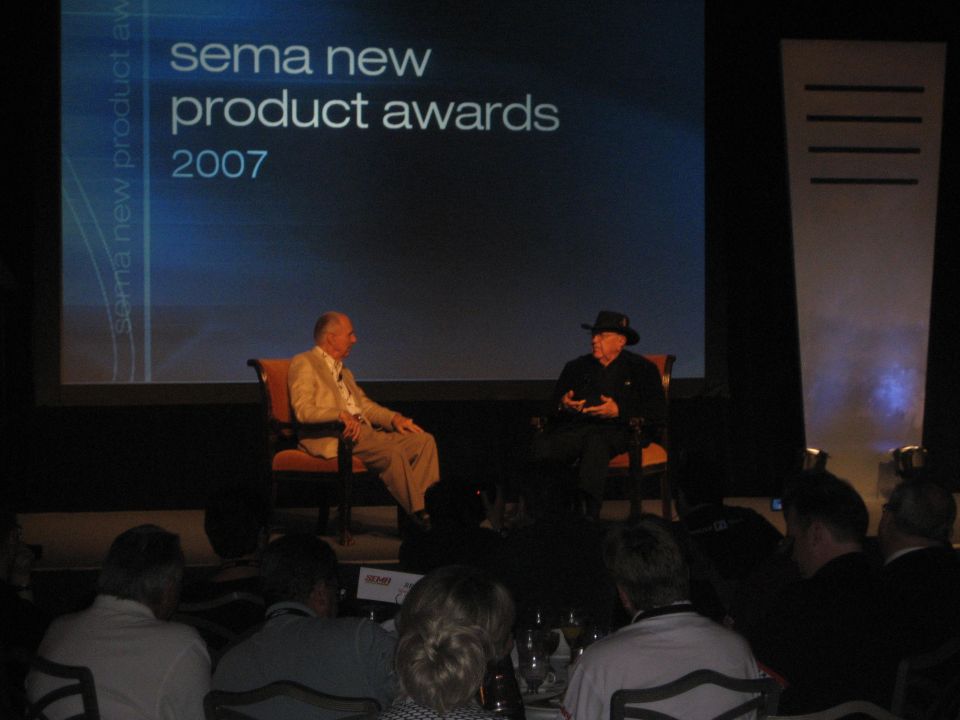 Two men seated on stage at SEMA New Product Awards 2007 before an audience