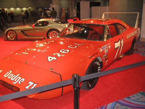 1998 Ford Crown Victoria - A vintage orange 1971 Dodge Charger Daytona race car, number 71, is displayed on a red carpet next to a modern silver sports car.