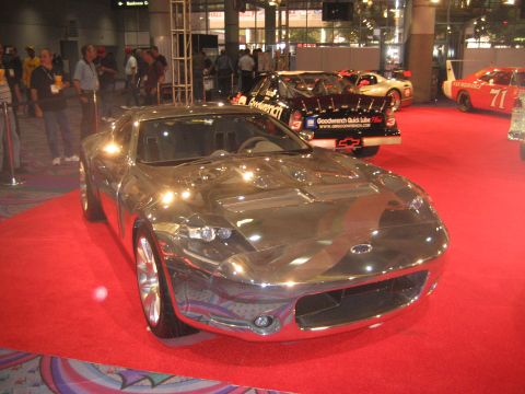 1998 Ford Crown Victoria - A chrome concept car is displayed on a red carpet at an indoor event with other vehicles visible.