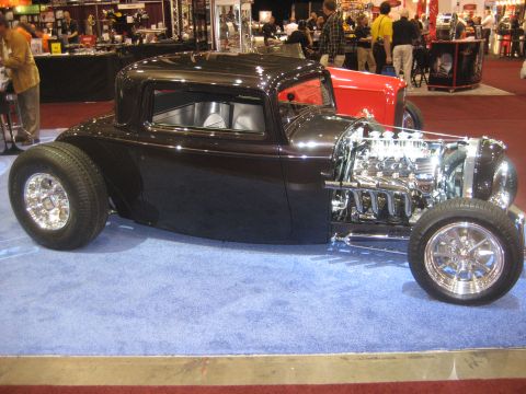 1998 Ford Crown Victoria - A custom black hot rod coupe is displayed indoors with its powerful V8 engine prominently visible.