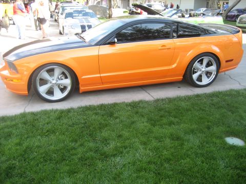 1998 Ford Crown Victoria - Side view of an orange Ford Mustang coupe with a black hood and roof, parked outdoors.