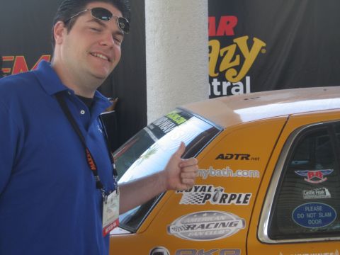 1998 Ford Crown Victoria - A man poses with a thumbs-up gesture beside a yellow vehicle adorned with various sponsor decals and a 'Please Do Not Slam Door' sticker.