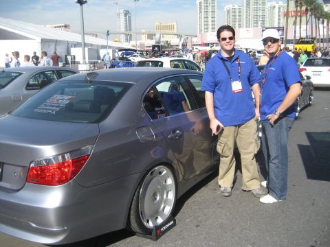 1998 Ford Crown Victoria - Two men stand next to a gray BMW 5 Series sedan at an outdoor event.