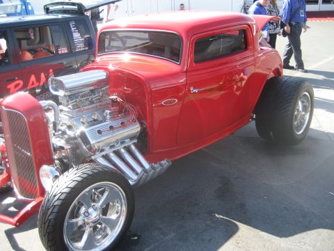 1998 Ford Crown Victoria - A custom red hot rod is displayed with its powerful engine exposed, parked beside another vehicle.