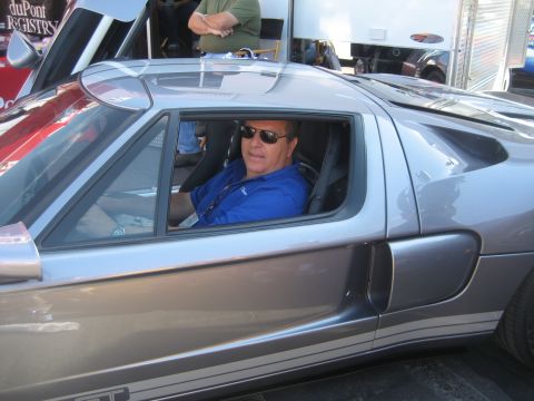 1998 Ford Crown Victoria - A man is seated inside a silver Ford GT sports car, with its door open.