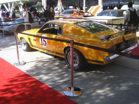 1998 Ford Crown Victoria - A yellow 1969 Ford Mustang Boss 302 race car is displayed on a red carpet with other vehicles in the background.
