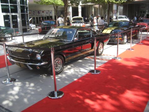 1998 Ford Crown Victoria - A black 1967 Ford Mustang GT-350 is displayed on a red carpet with other vehicles in the background.