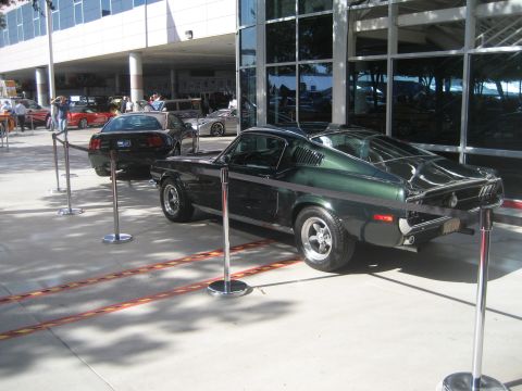 1998 Ford Crown Victoria - A classic Mustang is displayed with stanchions in front of a modern building with large windows.
