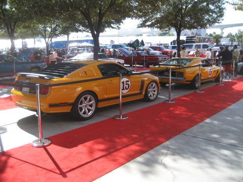1998 Ford Crown Victoria - Two yellow race cars are displayed on a red carpet with people in the background.