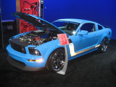 1998 Ford Crown Victoria - A blue 2005 Ford Mustang, identified by its 'BOSS 302' decal, is displayed with its hood open, revealing the engine.