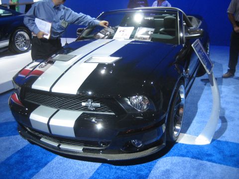 1998 Ford Crown Victoria - Black Ford Mustang convertible with silver racing stripes displayed indoors on a blue carpet.