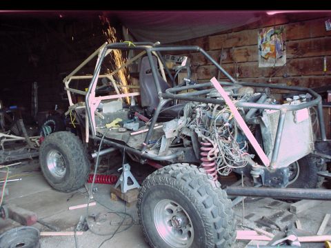 1984 Ford Bronco - A tube-frame buggy under construction in a wood-walled garage, its bare roll cage being welded with sparks flying, plus a single bucket sea…