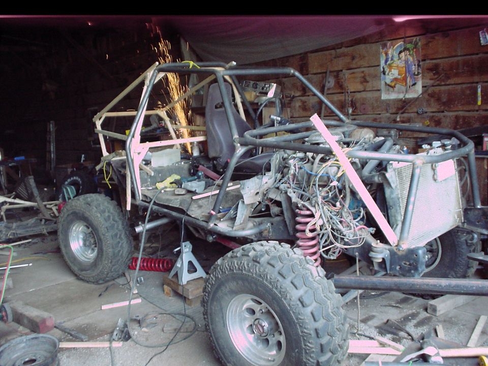 Tube-frame buggy build in a garage with welding sparks and exposed wiring