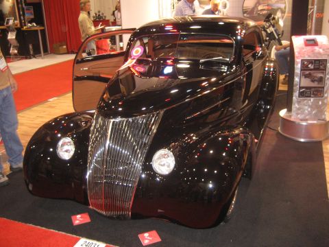 1998 Ford Crown Victoria - A gleaming black hot rod coupe with a prominent chrome grille and open suicide doors is displayed indoors.