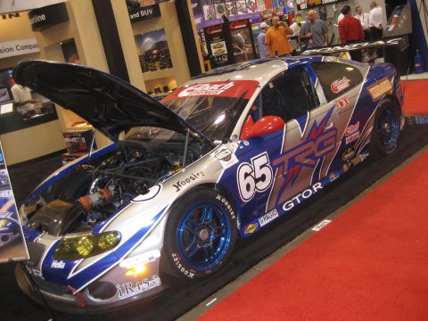 1998 Ford Crown Victoria - A race car with its hood open, displaying a blue and silver livery with the number 65, is shown on a red carpeted display.