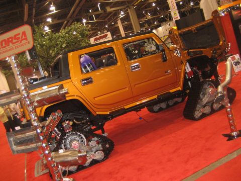 1998 Ford Crown Victoria - Modified Hummer H2 SUT with tracks and custom exhaust displayed indoors on a red carpet.