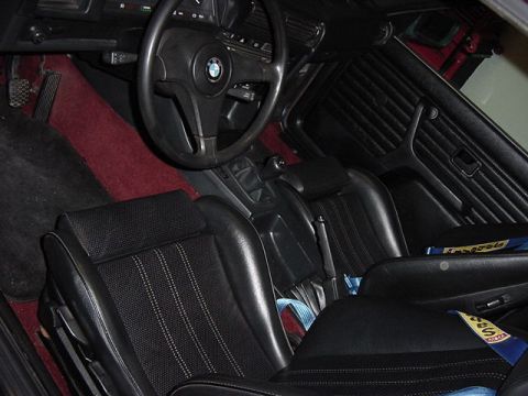 1984 BMW 3 Series - The interior of a 1984 BMW 3 Series shows black sport seats, a BMW steering wheel, and red carpeting.