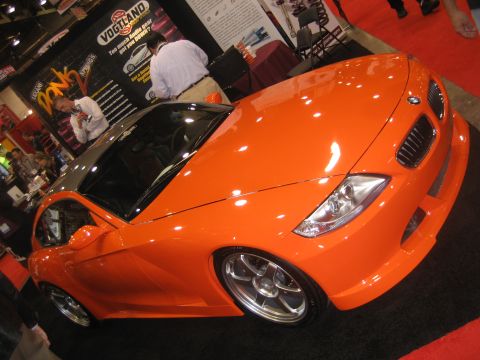 1998 Ford Crown Victoria - An orange sports car is showcased indoors with various vendor booths in the background.