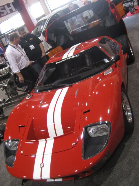 1998 Ford Crown Victoria - A red sports car with white racing stripes and a ROUSH decal is displayed at an event, with another vehicle and people in the background.