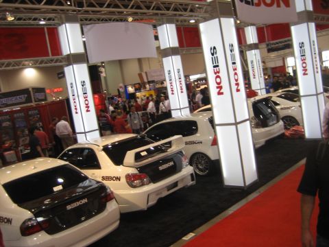 1998 Ford Crown Victoria - Multiple white cars, some with prominent spoilers and SEBON branding, are displayed indoors on a red carpet.