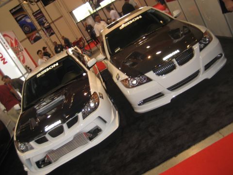 1998 Ford Crown Victoria - Two custom cars with aftermarket hoods are displayed at an indoor event.