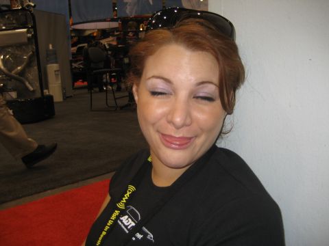 1998 Ford Crown Victoria - A woman playfully sticks her tongue out with her eyes closed, in what appears to be a trade show environment.