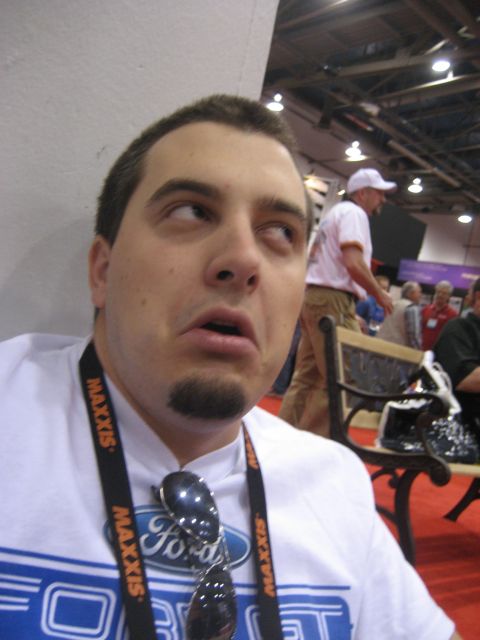 1998 Ford Crown Victoria - A man with a goatee and sunglasses looks upwards while wearing a white t-shirt with a Ford logo visible on a lanyard.