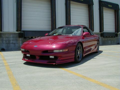 1994 Ford Probe - A red 1994 Ford Probe with a custom body kit is parked in front of a warehouse.