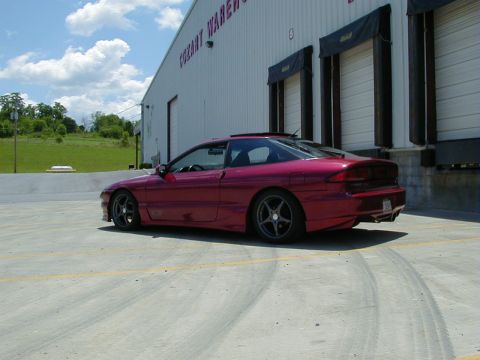 1994 Ford Probe - A red coupe is parked outside a warehouse with loading docks.