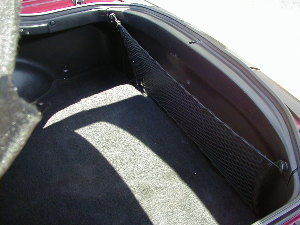 Car trunk with black carpet and a cargo net attached to the side