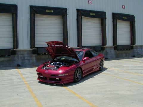 1994 Ford Probe - A red coupe with its hood open is parked in front of industrial loading docks.