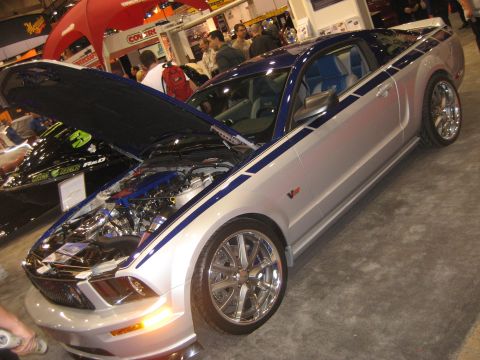 1998 Ford Crown Victoria - Silver Ford Mustang with blue racing stripes and a V6 emblem is displayed with its hood open.
