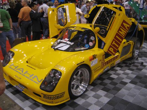 1998 Ford Crown Victoria - A bright yellow custom race car is displayed with its doors open, covered in various sponsor logos and branding.