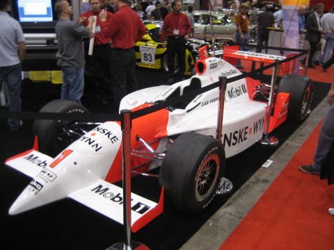 1998 Ford Crown Victoria - A white and orange IndyCar race car, identified as number 1 with Penske-Wynn sponsorship, is displayed indoors.