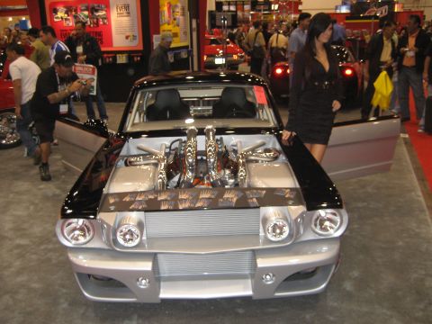 1998 Ford Crown Victoria - A customized classic car with its hood open, revealing a powerful V8 engine, is displayed at an auto show.