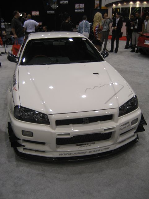 1998 Ford Crown Victoria - A white sports car with aggressive body modifications is displayed indoors, with people in the background.